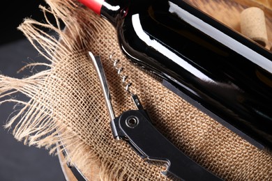 Sommelier knife with corkscrew, bottle of wine and wooden barrel on table, closeup