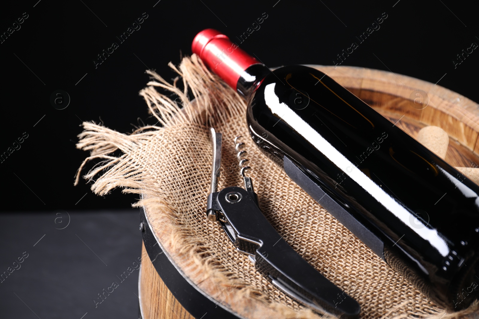 Photo of Sommelier knife with corkscrew, bottle of wine and wooden barrel on grey table, closeup