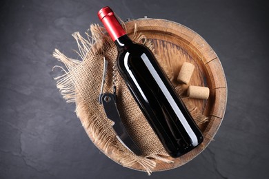 Photo of Sommelier knife with corkscrew, bottle of wine, corks and wooden barrel on grey table, top view