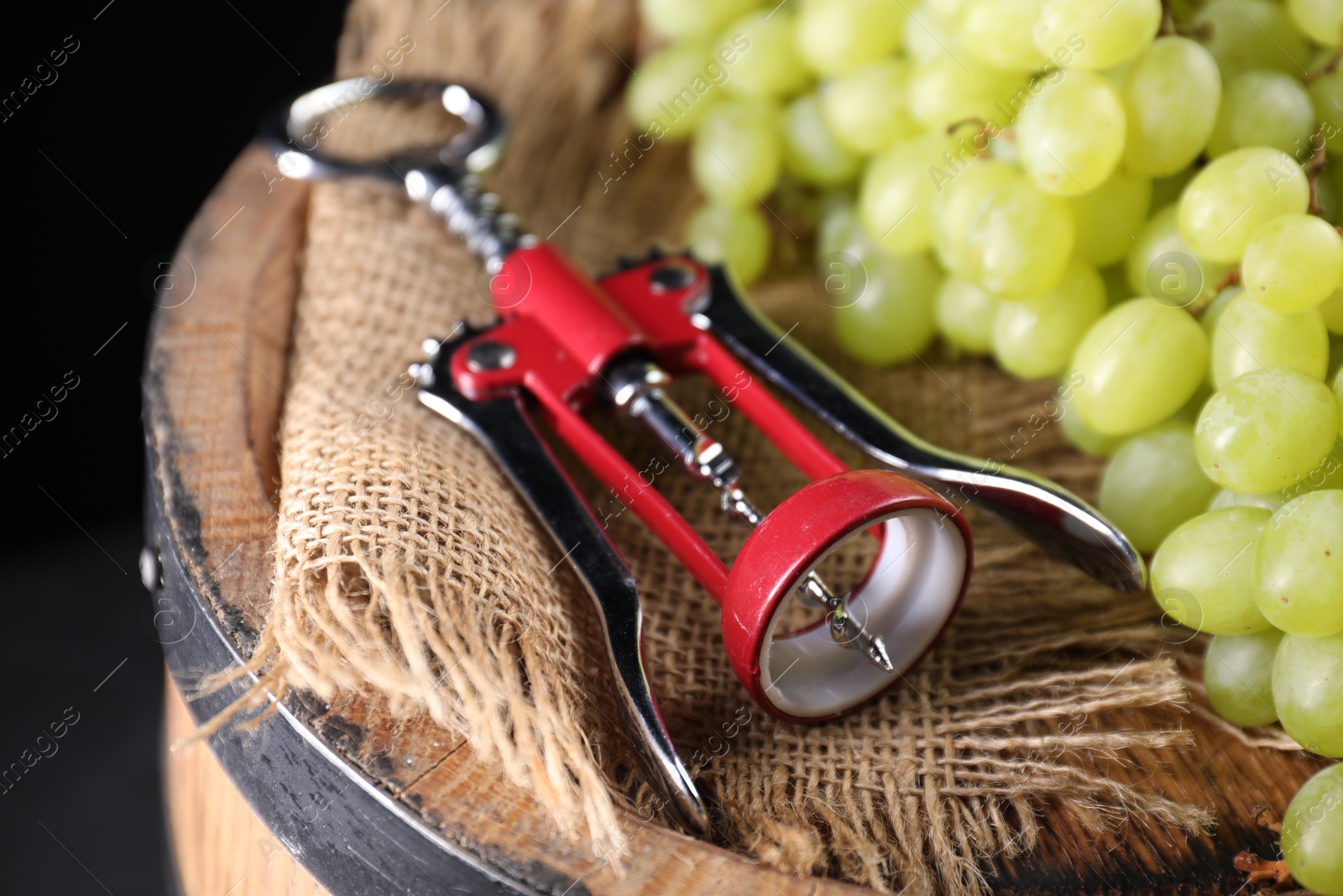 Photo of Wing corkscrew and grapes on wooden barrel, closeup