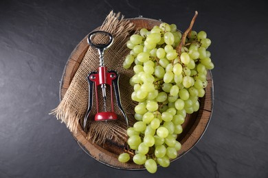 Photo of Wing corkscrew, grapes and wooden barrel on grey table, top view