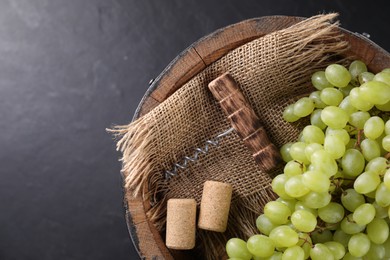 Photo of Corkscrew, corks, grapes and wooden barrel on grey table, top view. Space for text