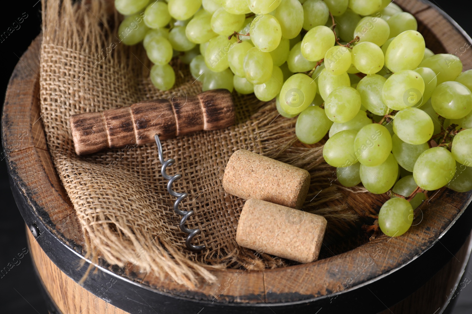 Photo of Corkscrew, corks and grapes on wooden barrel, closeup