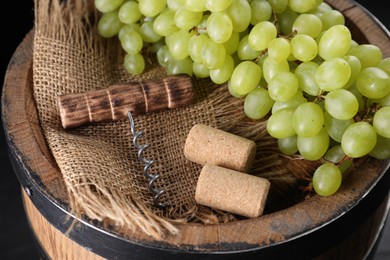 Corkscrew, corks and grapes on wooden barrel, closeup