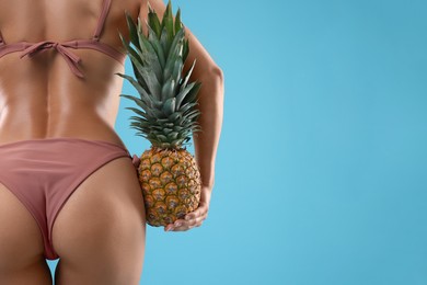 Woman in bikini with fresh pineapple on light blue background, closeup. Space for text