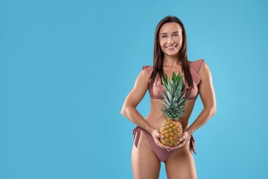 Photo of Woman in bikini with fresh pineapple on light blue background, space for text