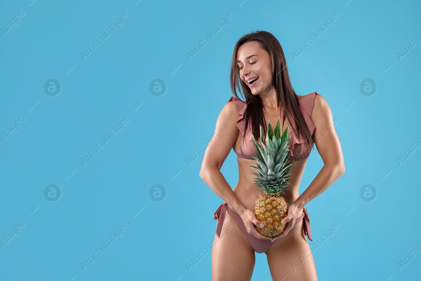 Photo of Woman in bikini with fresh pineapple on light blue background, space for text