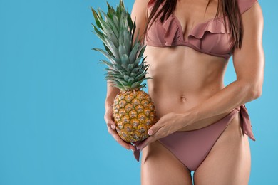 Woman in bikini with fresh pineapple on light blue background, closeup. Space for text