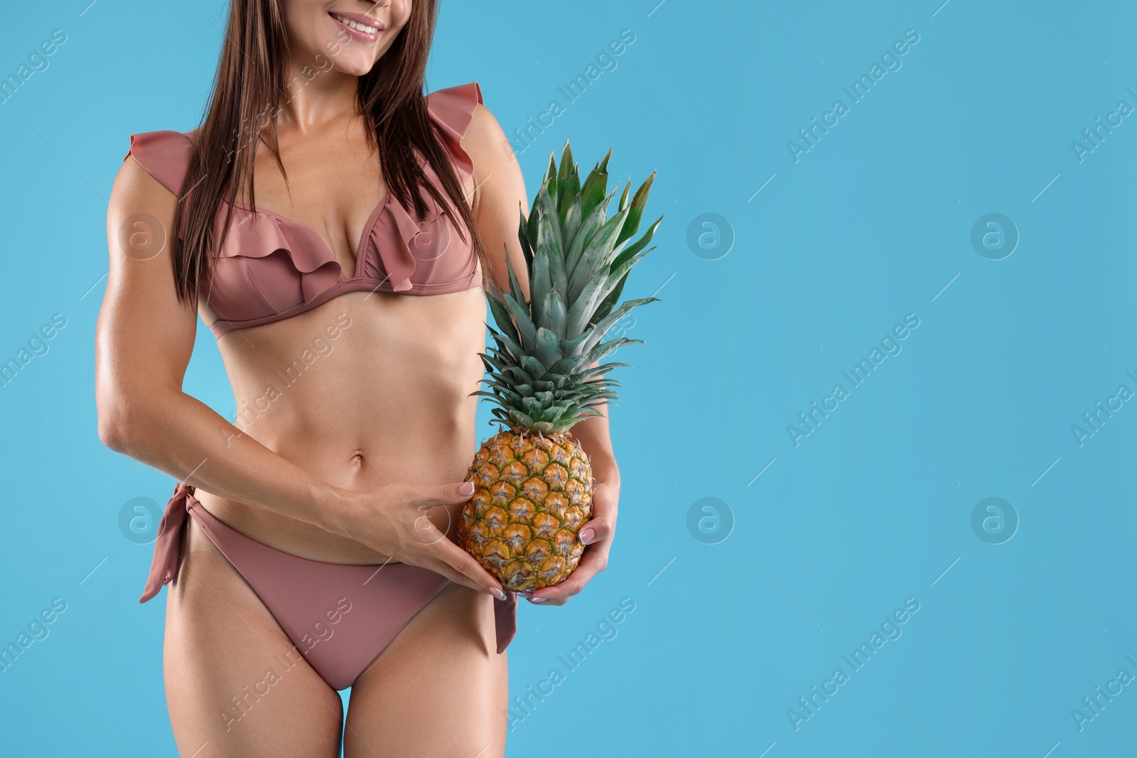 Photo of Woman in bikini with fresh pineapple on light blue background, closeup. Space for text