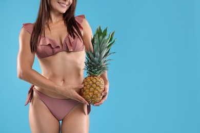 Woman in bikini with fresh pineapple on light blue background, closeup. Space for text