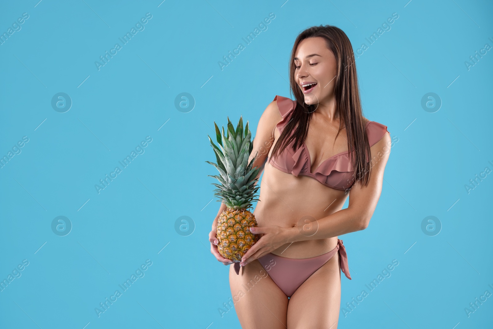 Photo of Woman in bikini with fresh pineapple on light blue background, space for text