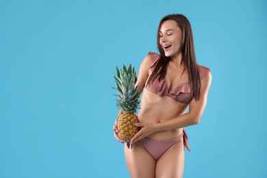 Woman in bikini with fresh pineapple on light blue background, space for text