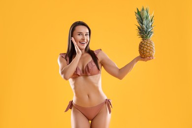 Photo of Woman in stylish bikini with fresh pineapple on orange background