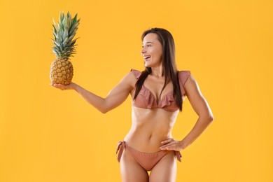 Photo of Woman in stylish bikini with fresh pineapple on orange background