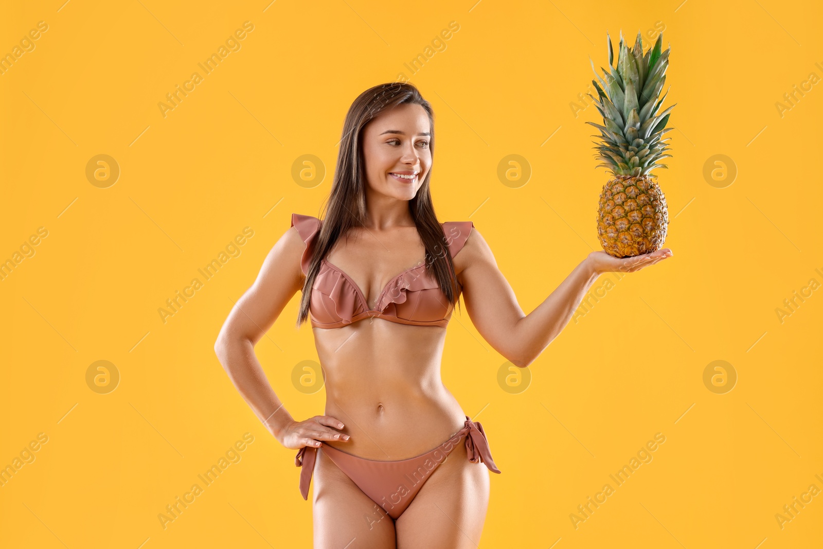 Photo of Woman in stylish bikini with fresh pineapple on orange background