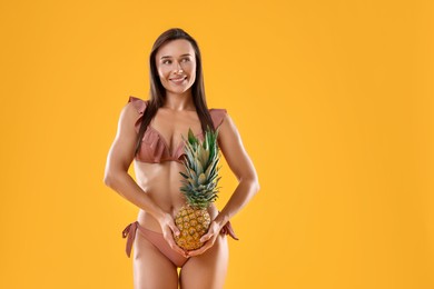 Woman in stylish bikini with fresh pineapple on orange background, space for text