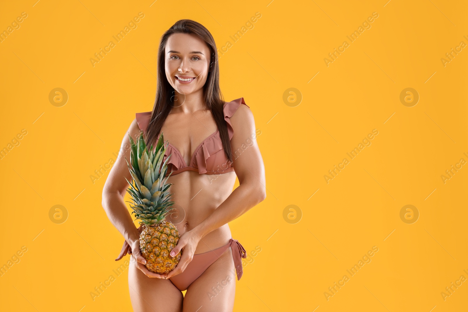 Photo of Woman in stylish bikini with fresh pineapple on orange background, space for text