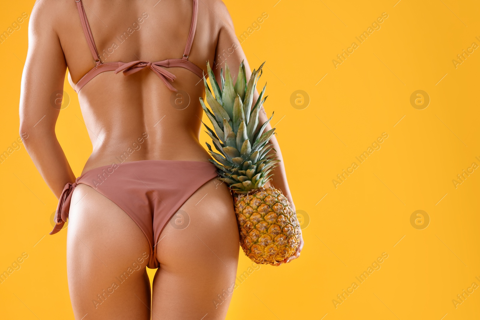 Photo of Woman in stylish bikini with fresh pineapple on orange background, closeup. Space for text