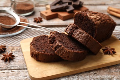 Photo of Delicious cut chocolate sponge cake and ingredients on wooden table, closeup