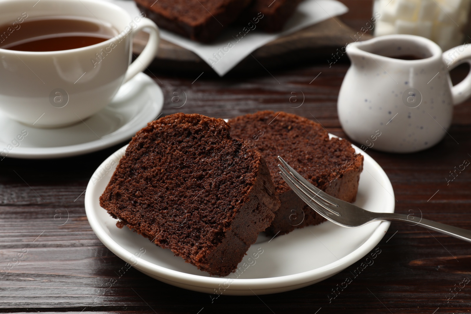 Photo of Slices of delicious chocolate sponge cake and tea on wooden table, closeup