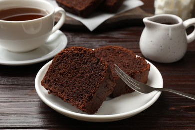 Photo of Slices of delicious chocolate sponge cake and tea on wooden table, closeup