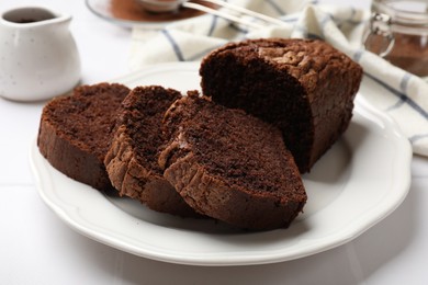 Photo of Delicious cut chocolate sponge cake on white tiled table, closeup