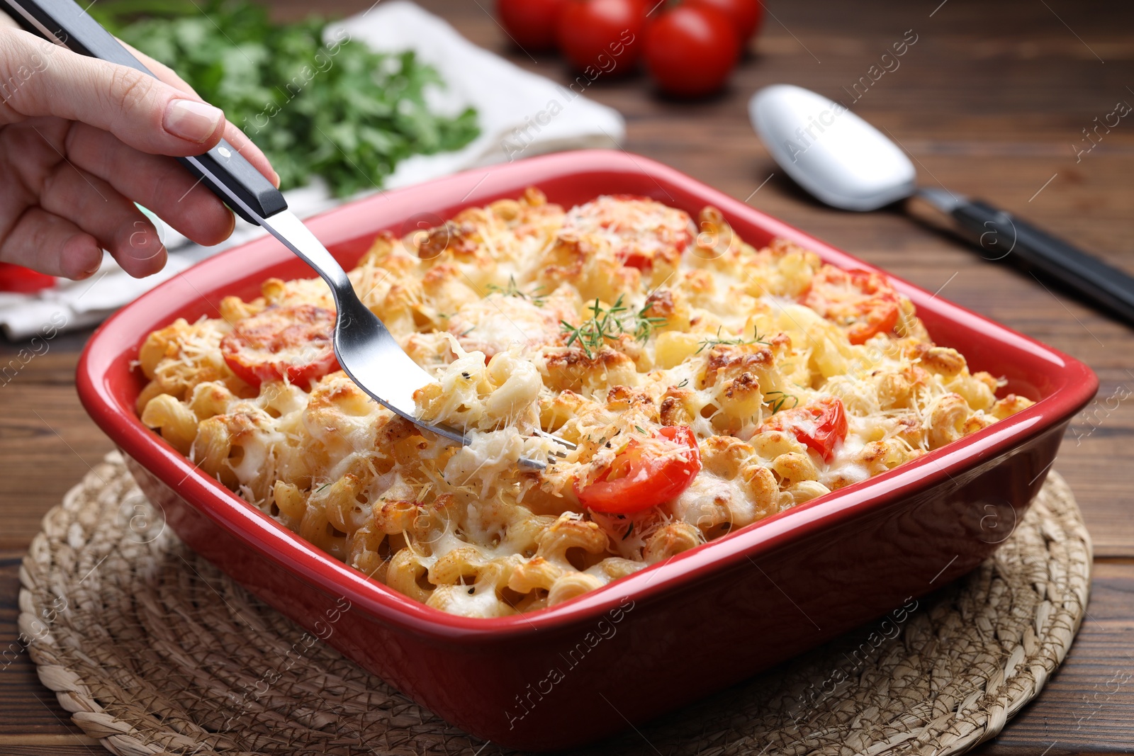 Photo of Woman eating delicious al forno pasta at wooden table, closeup