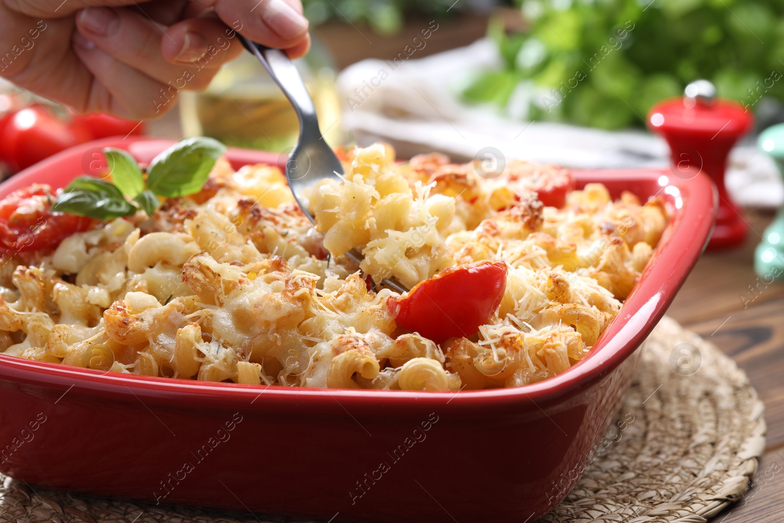 Photo of Woman eating delicious al forno pasta at wooden table, closeup