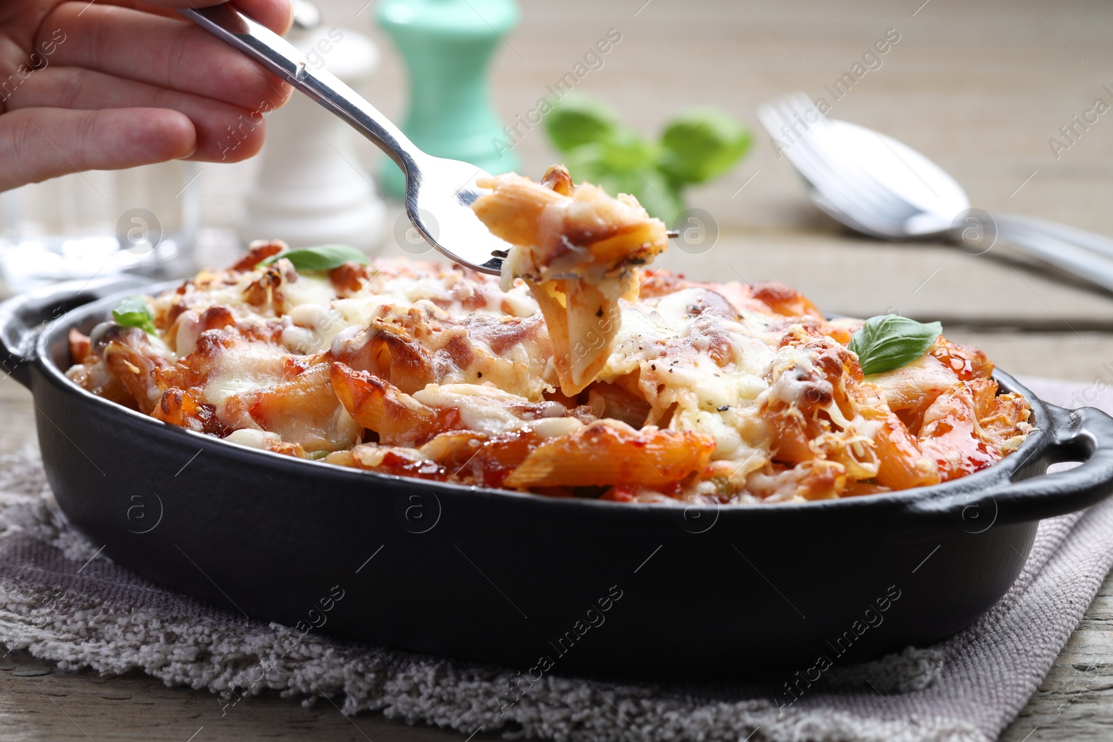 Photo of Woman eating delicious al forno pasta at wooden table, closeup