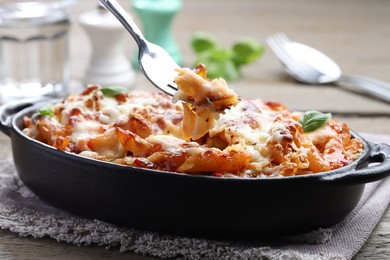 Photo of Eating delicious al forno pasta at wooden table, closeup