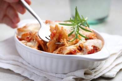 Photo of Woman eating delicious al forno pasta at light table, closeup