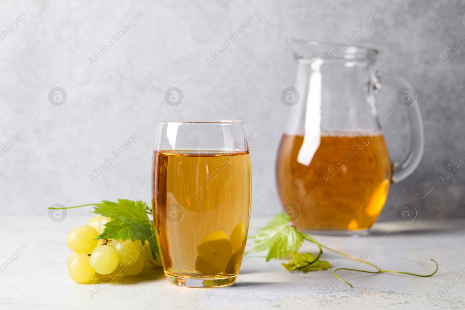 Photo of Tasty grape juice, leaves and berries on light textured table, closeup