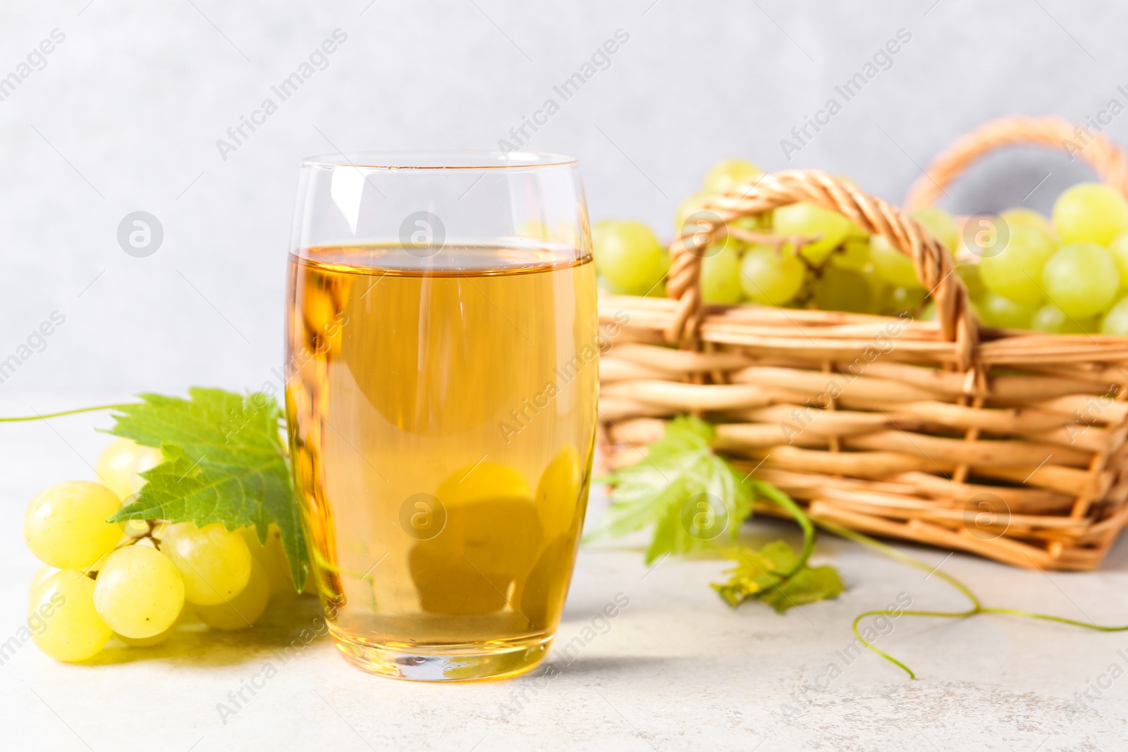 Photo of Tasty grape juice, leaves and berries on light textured table, closeup