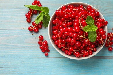 Fresh red currants in bowl and mint on light blue wooden table, top view. Space for text