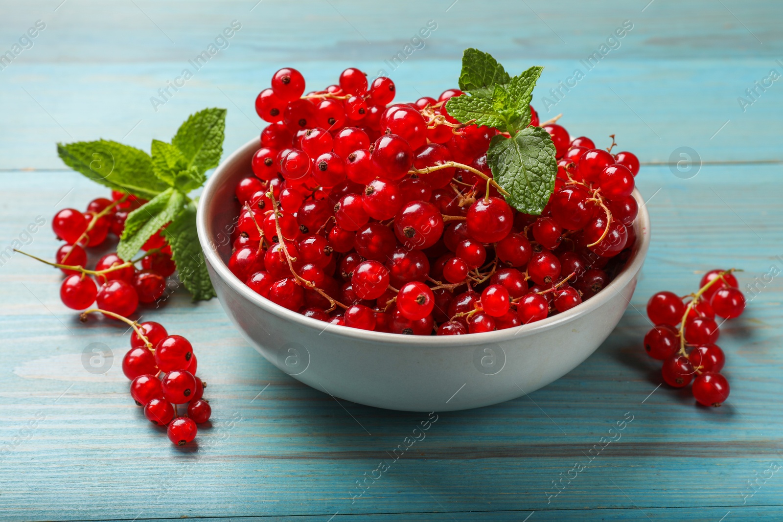 Photo of Fresh red currants in bowl and mint on light blue wooden table, closeup