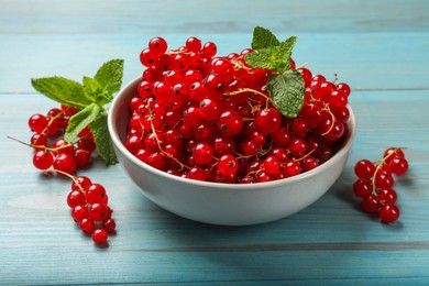 Photo of Fresh red currants in bowl and mint on light blue wooden table, closeup