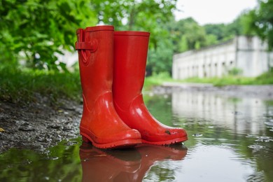 Photo of Red rubber boots in puddle at rainy day, closeup