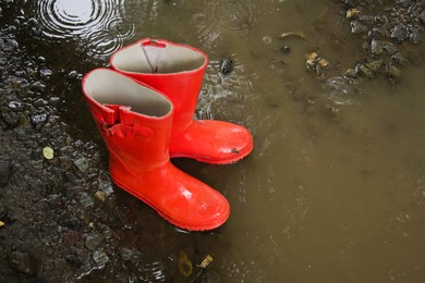 Photo of Red rubber boots in puddle at rainy day, above view