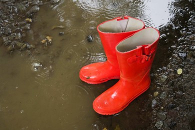 Photo of Red rubber boots in puddle at rainy day, above view