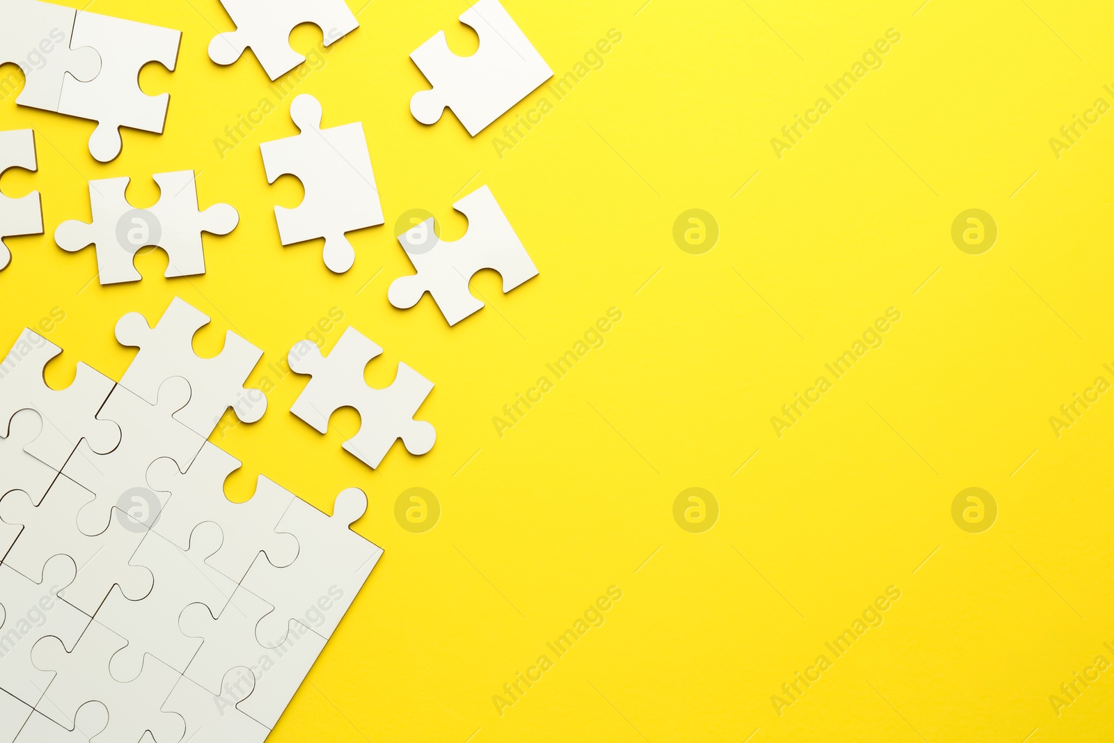 Photo of White puzzle pieces on yellow background, top view. Space for text