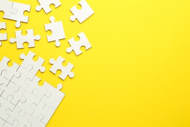 Photo of White puzzle pieces on yellow background, top view. Space for text