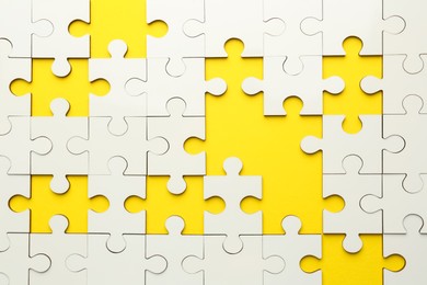 Photo of White puzzle with missing pieces on yellow background, top view