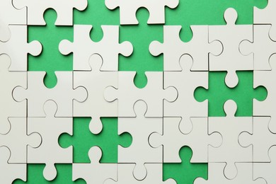 Photo of White puzzle with missing pieces on green background, top view