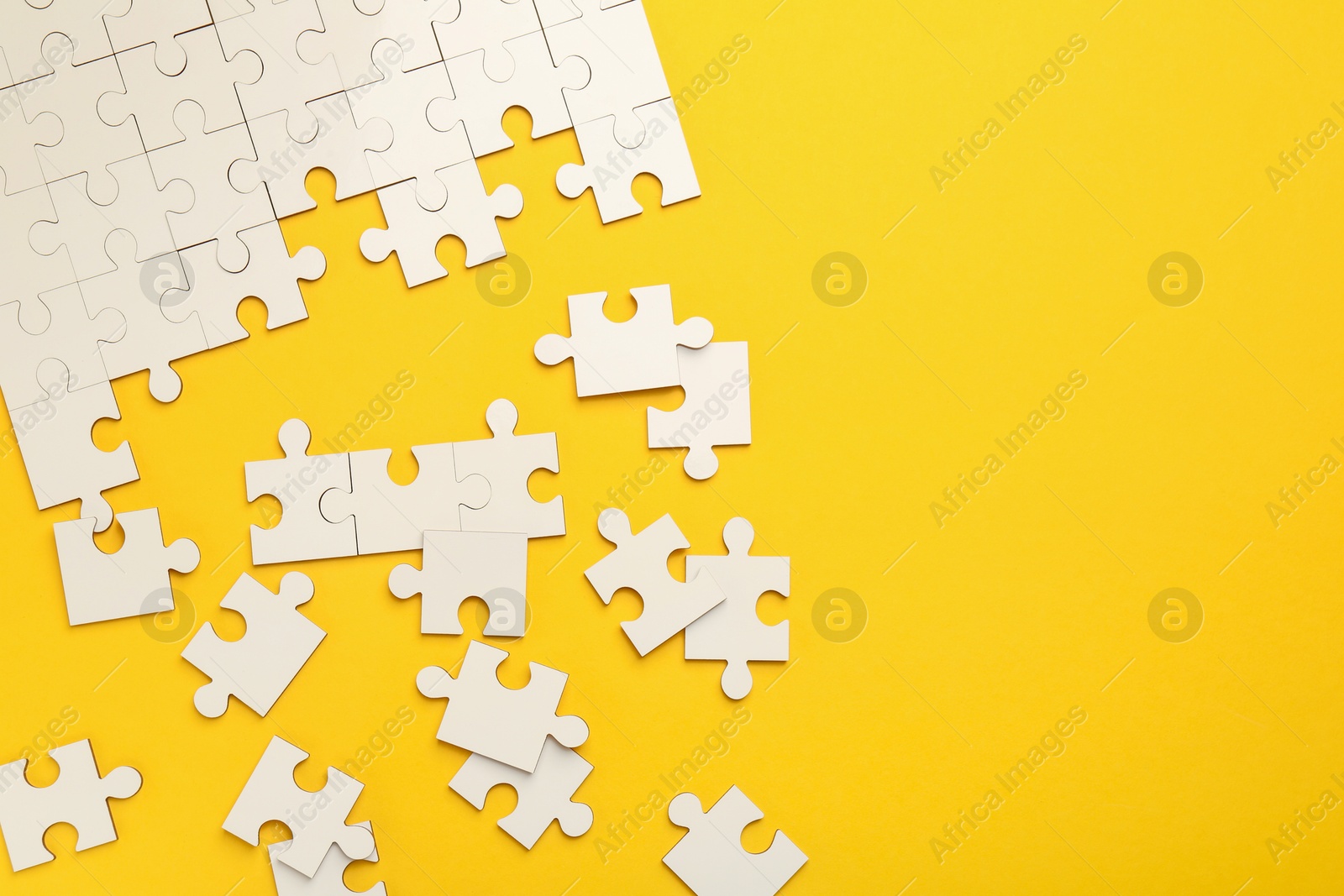 Photo of White puzzle pieces on yellow background, top view. Space for text