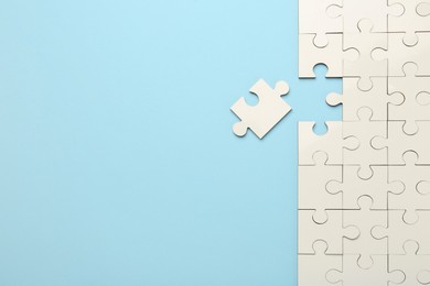 Photo of White puzzle pieces on light blue background, top view. Space for text