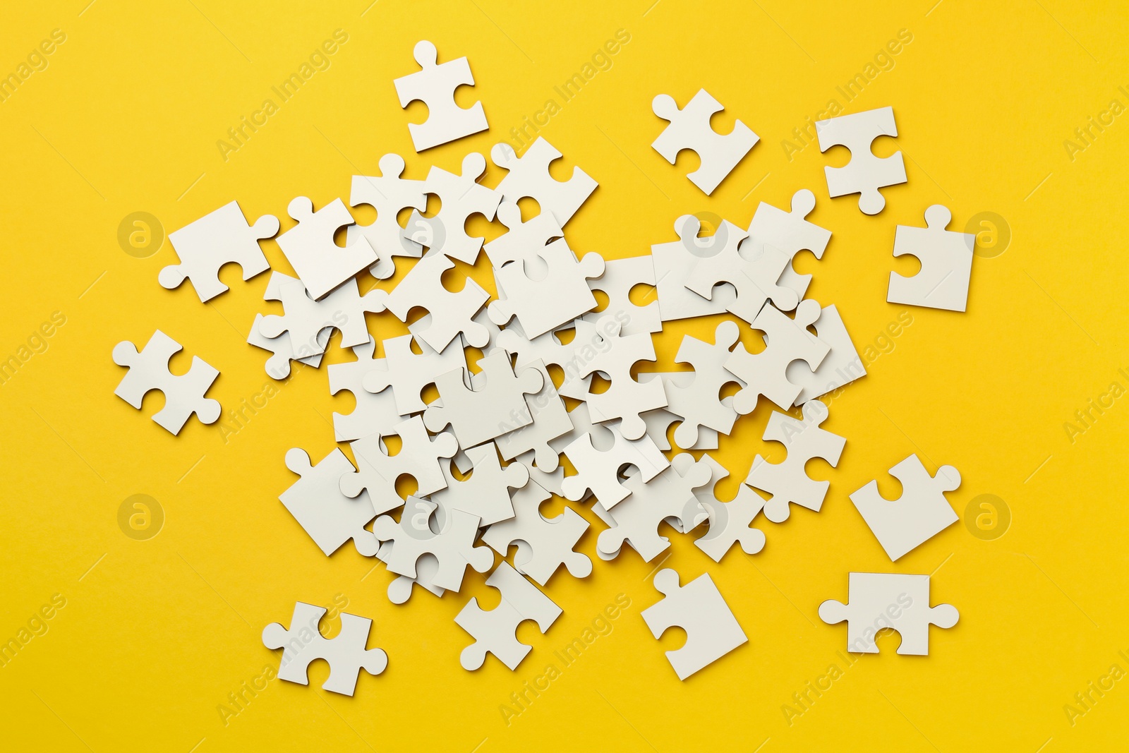 Photo of White puzzle pieces on yellow background, top view