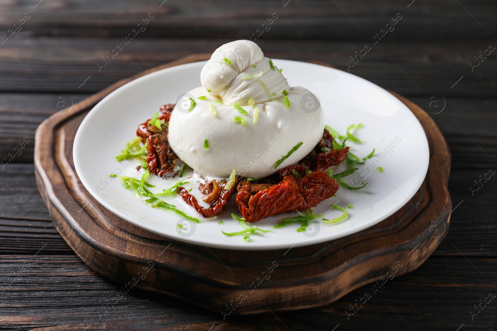 Photo of Delicious burrata cheese and sun-dried tomatoes on wooden table, closeup