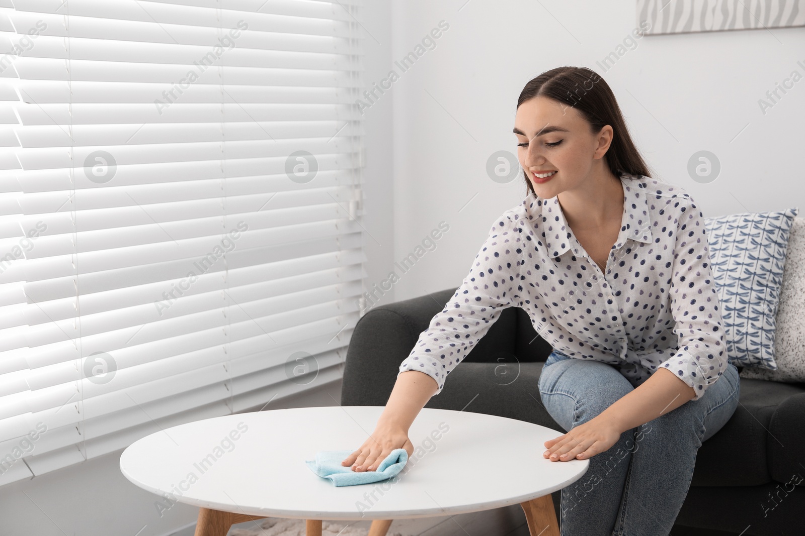 Photo of Beautiful young woman wiping coffee table with rag at home