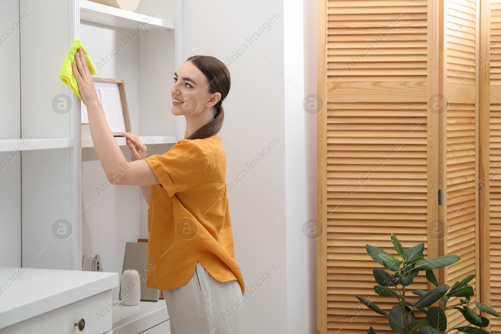 Photo of Beautiful young woman cleaning furniture with rag at home