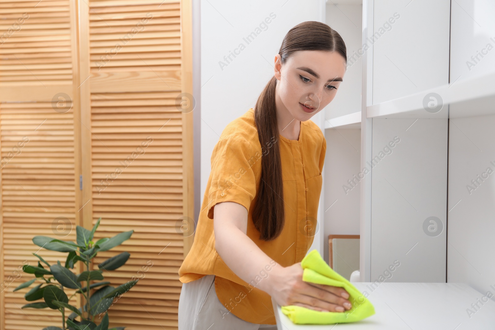 Photo of Beautiful young woman cleaning furniture with rag at home